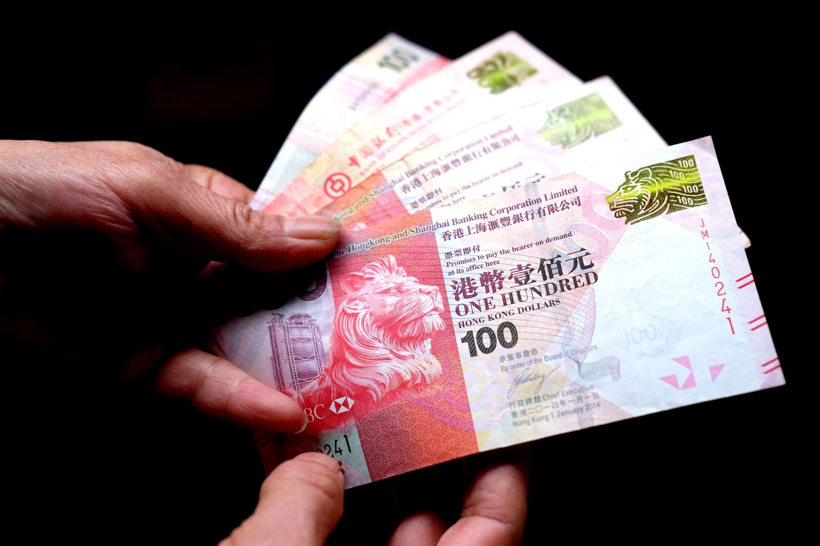 Closeup shot of a person holding Hong Kong dollars in front of a black background